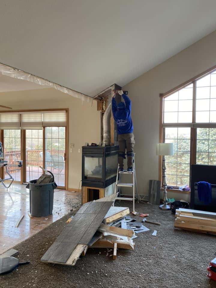 Worker removing existing gas fireplace and ductwork during demolition with torn-out flooring and debris on floor